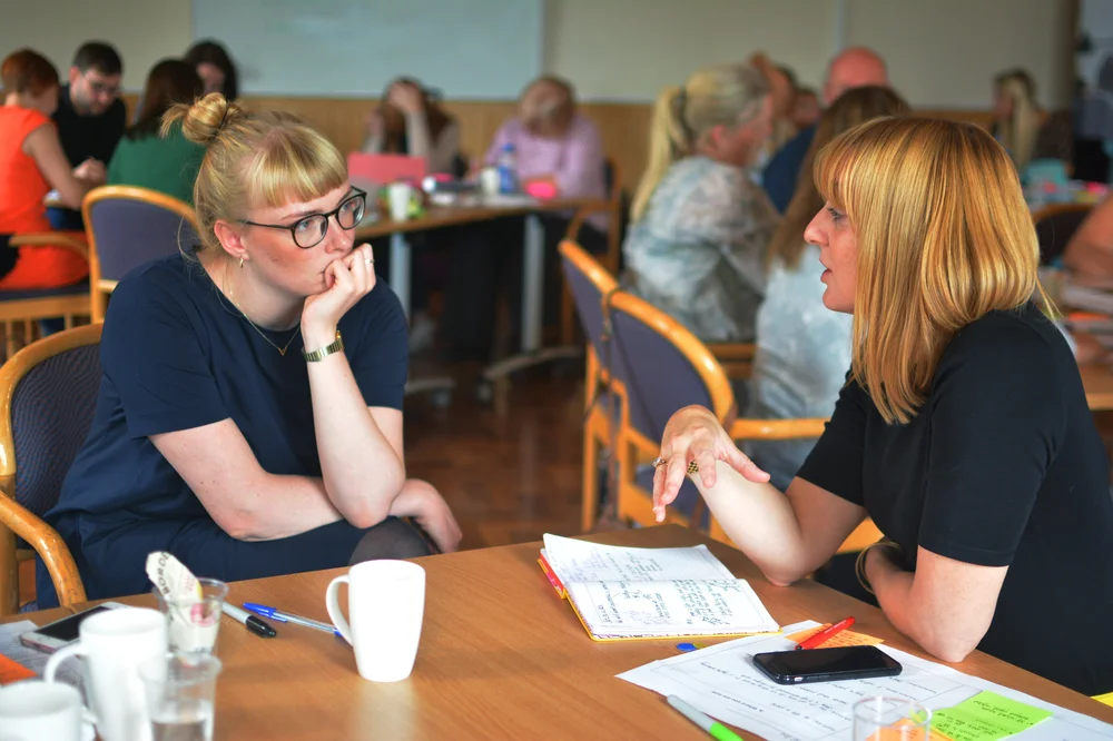 Churchill Fellow Alice Stott sat at a table engaged in conversation with another woman
