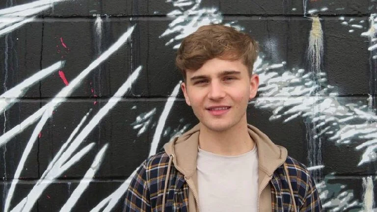 Churchill Fellow Callum Lynch stood in front of a black wall with art