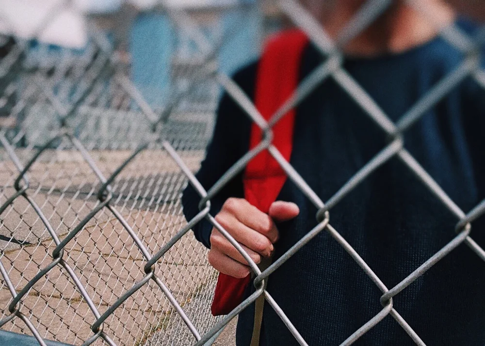 Young bog standing behind a fence holding backpack