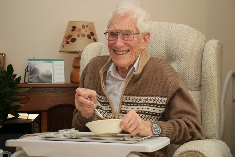 Elderly white man sitting in an arm chair with a bowl of food