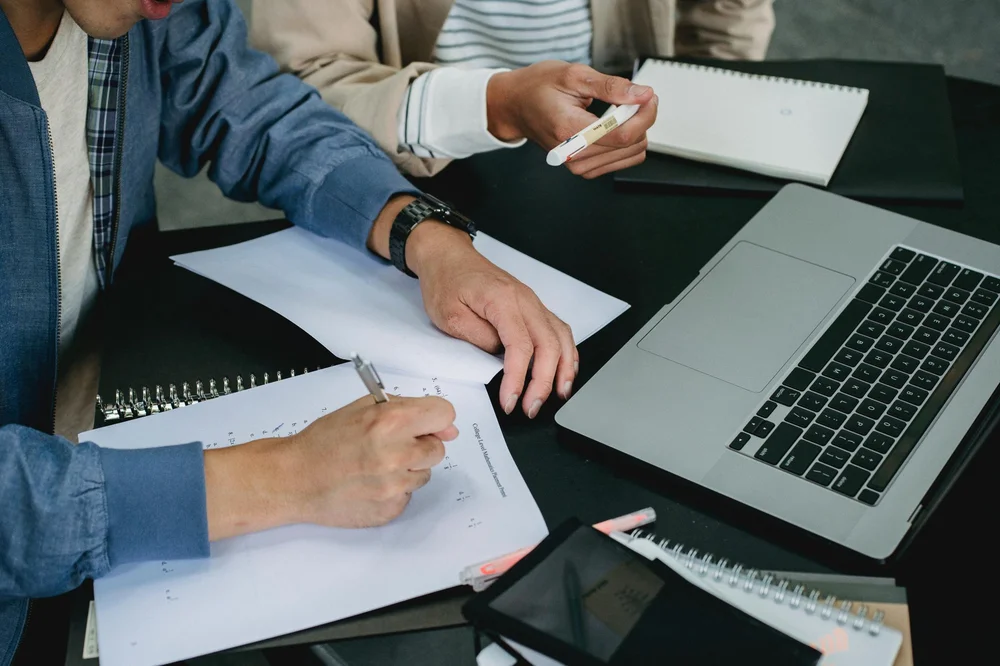 Two people sitting at a desk with laptops taking notes