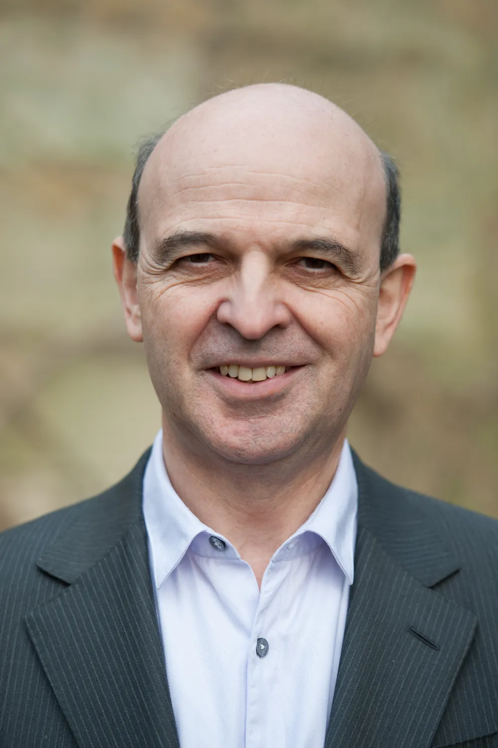 An older gentleman wearing a suit jacket and open neck shirt smiling at the camera
