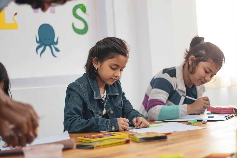 Two school children sat at a table writing on paper